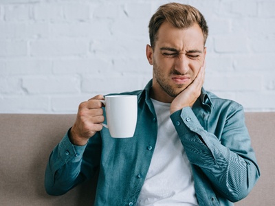 person drinking coffee and holding their jaw in pain